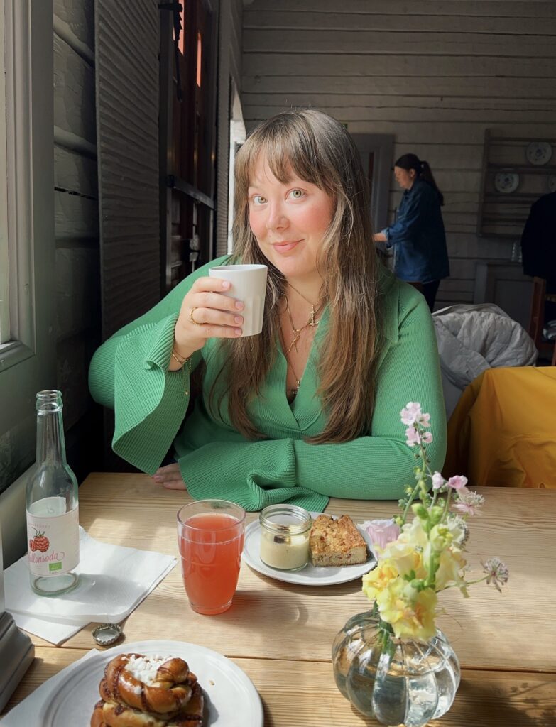 Bild på Ebba Thorolvsen, på ett café. Hon håller i en kaffe och ser in i kameran.